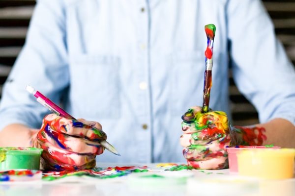 Stock image of a man holding paintbrushes and covered in paint